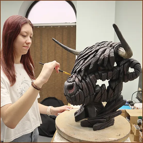 Holly painting by hand a black Highland Cow sculpture.
